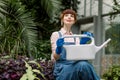 Gardening woman with watering can in greenhouse. Pretty woman agronomist sitting with watering can in modern hothouse Royalty Free Stock Photo