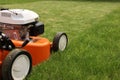 Gardening work tools. Close up details of orange electric lawn mower, wheels, motor on bright lush green grass. Rotary