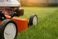 Gardening work tools. Close up details of orange electric lawn mower, wheels, motor on bright lush green grass. Rotary