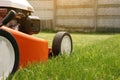 Gardening work tools. Close up details of orange electric lawn mower, wheels, motor on bright lush green grass. Rotary