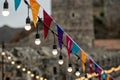 Garland of colorful flags and glowing light bulbs against a defocused background of castle Royalty Free Stock Photo
