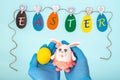 Garland of paper eggs with the inscription EASTER and hands in medical gloves holding a yellow egg and bunny Royalty Free Stock Photo