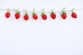 Garland of red ripe strawberries hanging on wooden clothespin on rope twine, located on top edge on white wood background. Copy Royalty Free Stock Photo