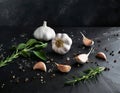 Garlic, garlic cloves surrounded by herbs and spices, on a black stone table