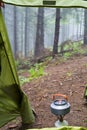 Gas burner with a tourist kettle near a tourist tent on a background of foggy coniferous forest in the mountains. Outdoor tourism