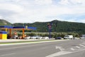 a gas station with two rows of parked cars and mountains in the background