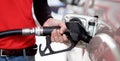 Gas station worker in red uniform filling up bronze pickup truck tank. Closeup hand holding black gas pump nozzle Royalty Free Stock Photo