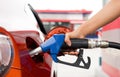 Gas station worker`s hand holding blue benzene gas pump, filling up red sport car tank. Close up