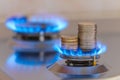 Gas stove lit, with stacks of coins above it. Increase in gas costs and tariffs. Royalty Free Stock Photo