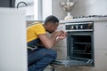 Dark-skinned service man in yellow tshirt repairing the gas stove Royalty Free Stock Photo