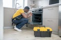 Dark-skinned service man in yellow tshirt repairing the gas stove