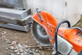 A gasoline cutter with a diamond cutting wheel in front of a construction site and concrete parapets