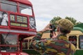 Man holding a camera and taking a photograph of a red London Routemaster classic bus