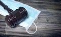 Gavel Resting On A Protective Mask on a wooden table.