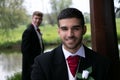 Gay couple of grooms pose for photographs by a lake on their wedding day