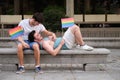 Gay couple laughing and hugging sitting on a bench holding LGBT flags. Royalty Free Stock Photo