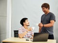 Gay couple in office. Attractive Asian men drinking coffee together working laptop computer at offic