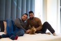 Gay couple sitting on the bed playing with their pet. They are looking at camera happy Royalty Free Stock Photo