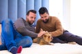 Gay couple sitting on the bed playing with their pet. They are looking at the dog with affection Royalty Free Stock Photo