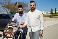 Gay couple and their young daughter taking a walk in the park. The little daughter is riding in the carriage