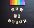 Gay is Great word tiles LGBTQ+ on a black background with a rainbow flag