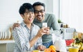 Gay LGBT sweet Asian couple wearing pajamas, smiling, with happiness and love while making and pouring juice smoothie to glass and Royalty Free Stock Photo