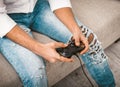 Gay playing computer game. Young man in jeans holds Play Station joystick sitting at couch. Close up shot of male hands Royalty Free Stock Photo