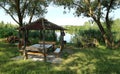 Gazebo with ornamental rustic wooden benches as support poles on the banks of the river at dawn