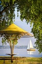 Gazebo surrounded by tree golden branches on the bay with sailing yacht on the horizon. Autumn landscape, sunny day. Royalty Free Stock Photo