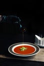 Gazpacho diet tomato soup with herbs and cucumber on a plate. woman`s hand fills the finished soup with olive oil