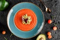 Gazpacho tomato cream soup in plate with avocado and greens over dark background.