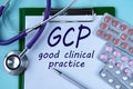 GCP - acronym on a white piece of paper on a blue background. A stethoscope and pills lie side by side