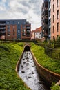 Small water stream with few decorative stones inside next to modern estate buildings with green