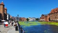 View of the old city of Gdansk on the Motlawa River. Tourists walk along the waterfront. On Motlawa green patches of duckweed.