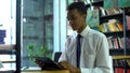 Geek mixed-race male student doing homework online, using tablet pc at library Royalty Free Stock Photo