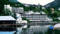 Geiranger, Norway - 15 Jun 2019: Motels, homes and other buildings are reflected in the fjord water near shore.