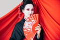 Geisha in black kimono with hand fan and red cloth on background isolated on white