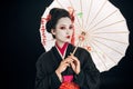 Geisha in black kimono with red flowers in hair holding asian umbrella isolated on black Royalty Free Stock Photo