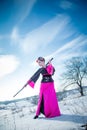 Geisha with katana in black and pink kimomo on winter landscape and blue sky background. Royalty Free Stock Photo