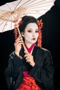 Geisha in kimono with red flowers in hair holding traditional asian umbrella isolated on black Royalty Free Stock Photo