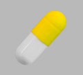 A gelatin capsule with yellow cap on grey background closeup Royalty Free Stock Photo