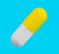 A gelatin capsule with yellow cap isolated on a blue background closeup Royalty Free Stock Photo