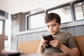 Gen Z preteen school kid using learning app on smart phone Reading book online for school homework,Young boy browsing Internet,or Royalty Free Stock Photo