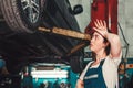 Gender equality. A young brunette woman in uniform stands near the lift with the car, and looks at the wheel, wiping the sweat