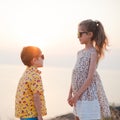 Gender relationship concept of happy little kids boy and girl look at each other through summer sunglasses on sea beach in sunset Royalty Free Stock Photo