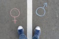 Gender symbol of a man and a woman drawn in chalk on the asphalt. A man`s feet stand on the road markings between the gender