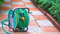 The old water hose reel agriculture accessory with nozzle on stone pavement tile floor in home gardening area Royalty Free Stock Photo