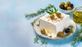 Tasty feta cheese with olives and herbs on light blue background with copy space