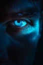 Glowing blue eye of a mysterious man. Serious expression. Evil man in the dark. Royalty Free Stock Photo