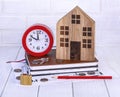Home loan concept. Wooden house, red alarm clock, house keys, coins, stationeryGenerated image
